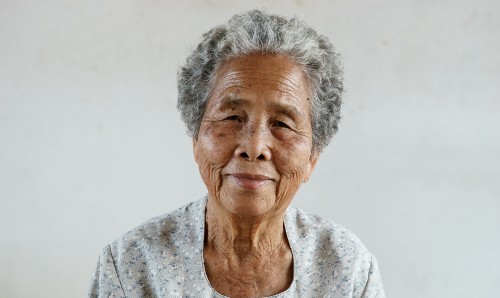An older Chinese lady smiling at the camera, in front of a white background.