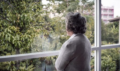 An elderly Asian senior woman with grey hair looking out the window.