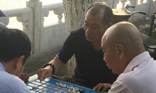 A group of Chinese men playing a board game outside.