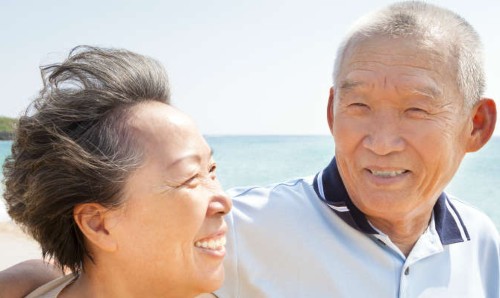 An older couple walking on a beach, smiling.