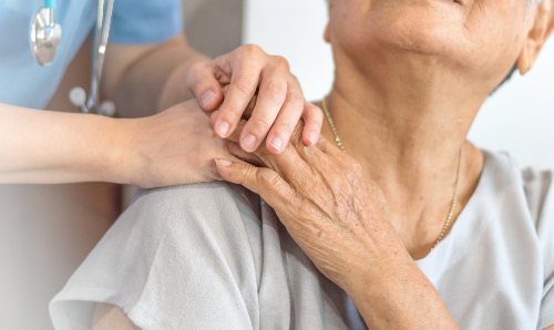 A medical professional holding the hand of an elderly lady.